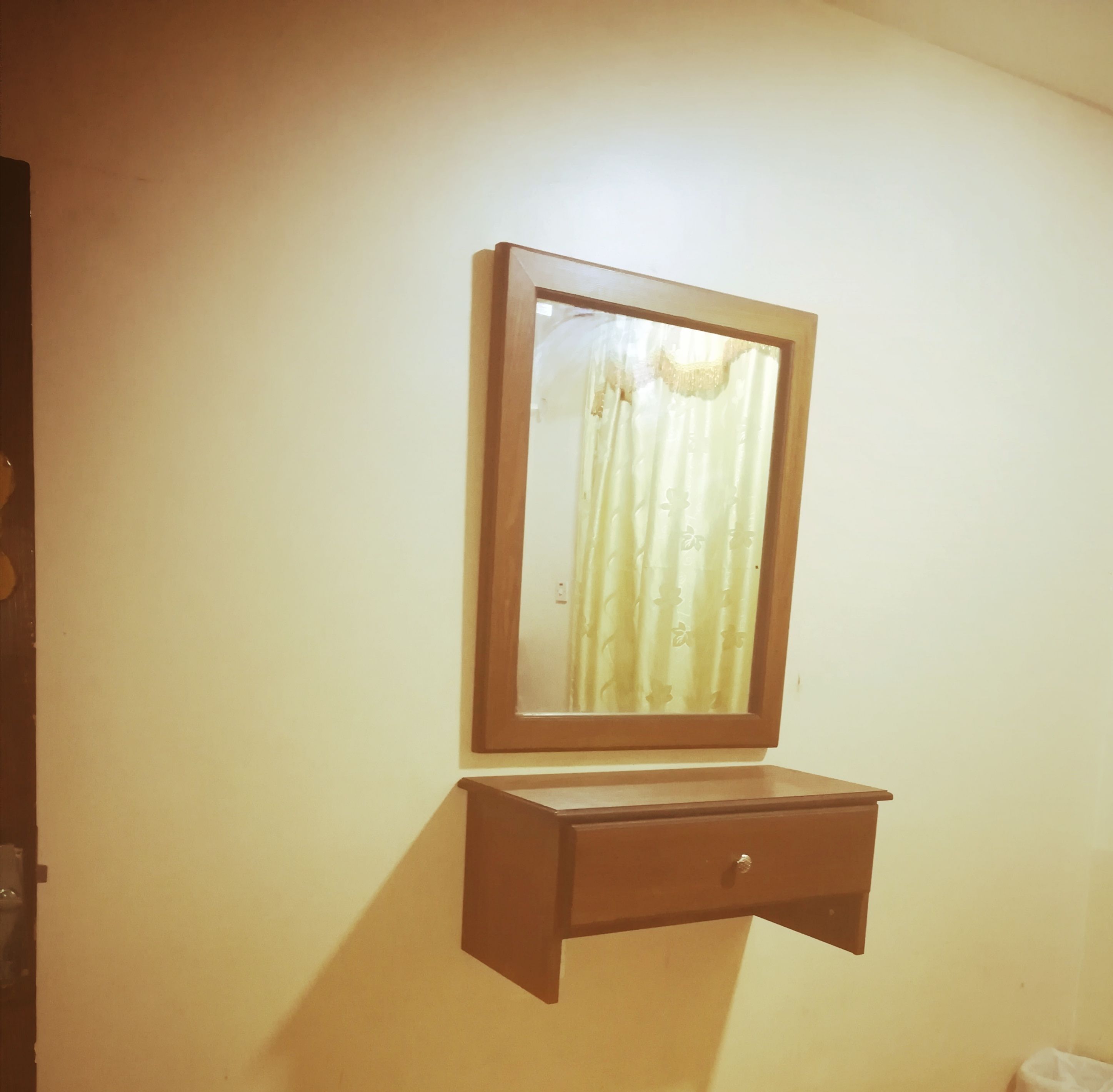 Uno specchio con cornice in legno montato su una parete, sopra un comò con un cassetto.
