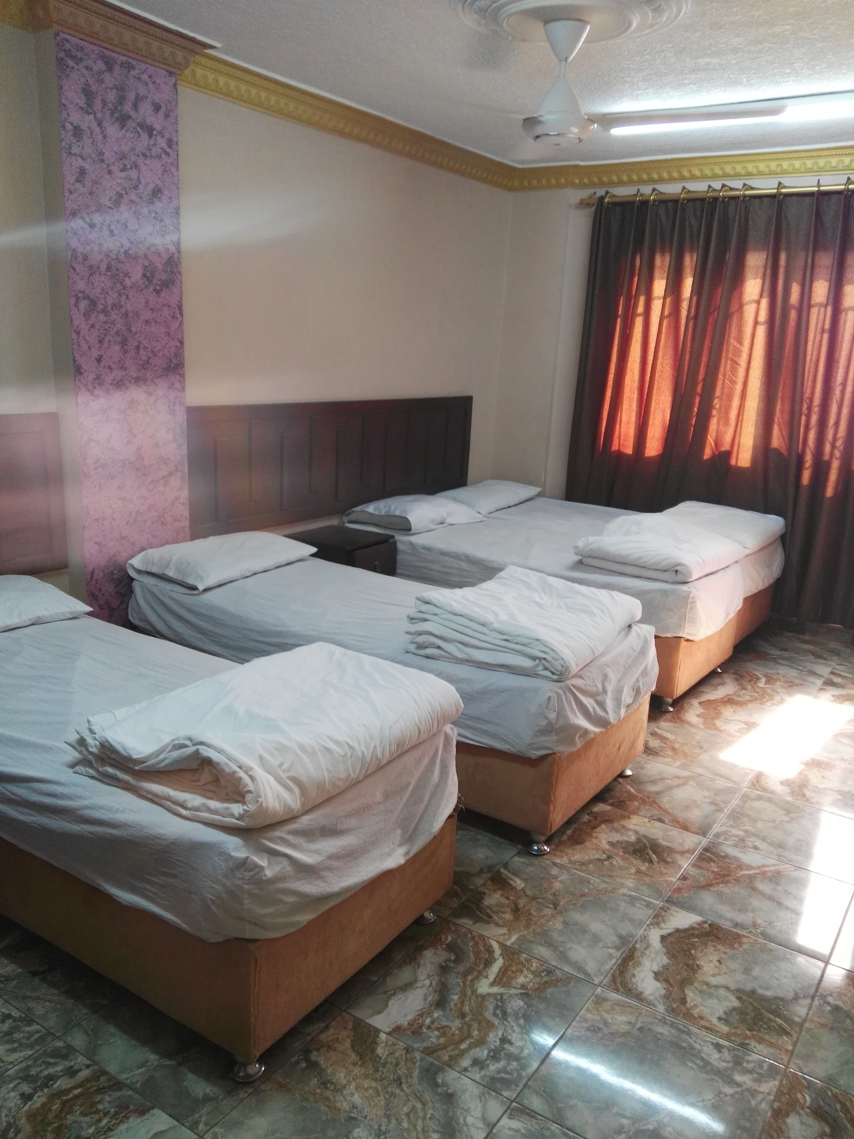 A hotel room with four beds, a marble-tiled floor, a ceiling fan, and a window with curtains.