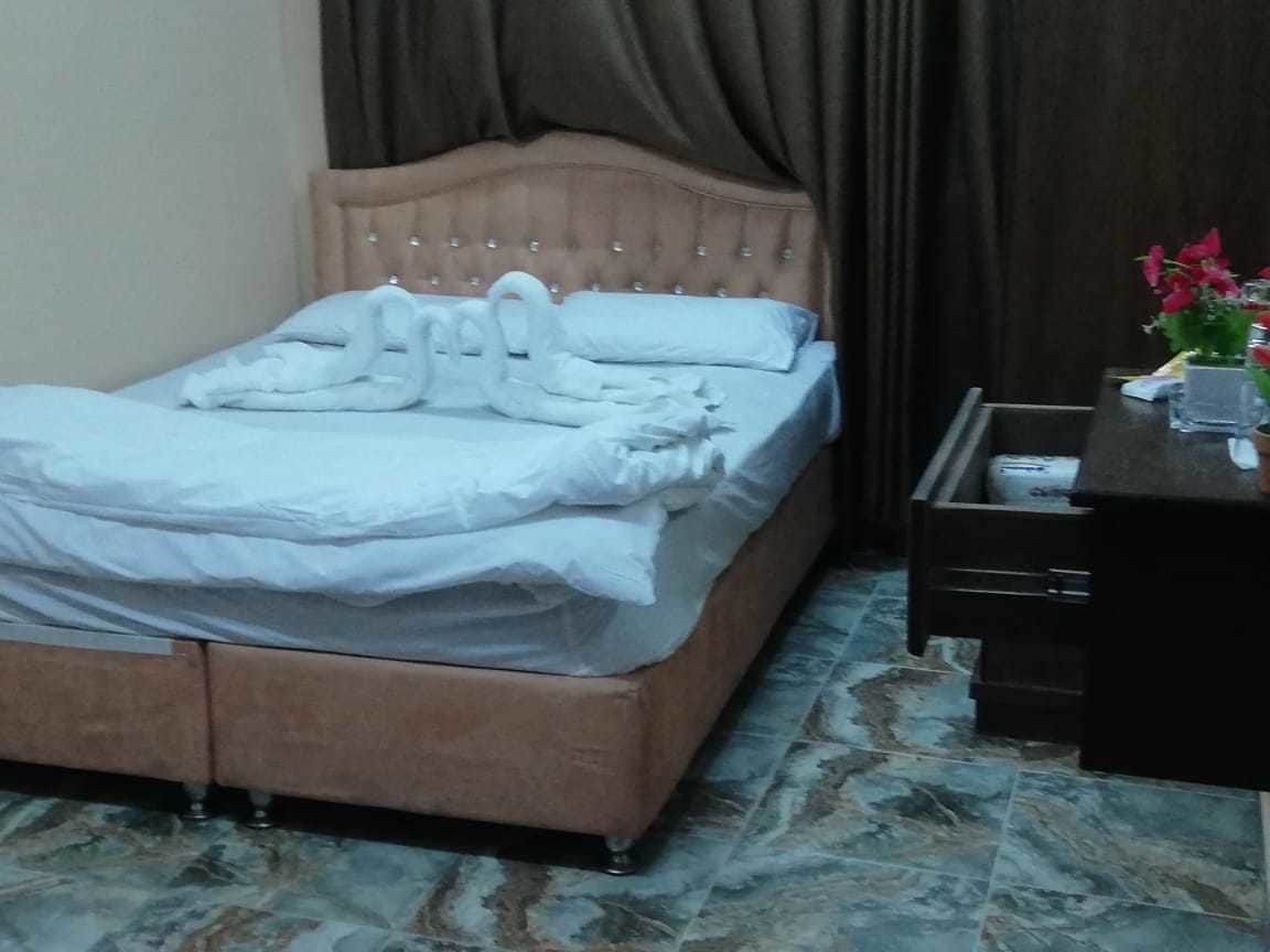 Cama bem arrumada com cabeceira, mesa de cabeceira com um vaso de flores e um aparador de madeira escura.