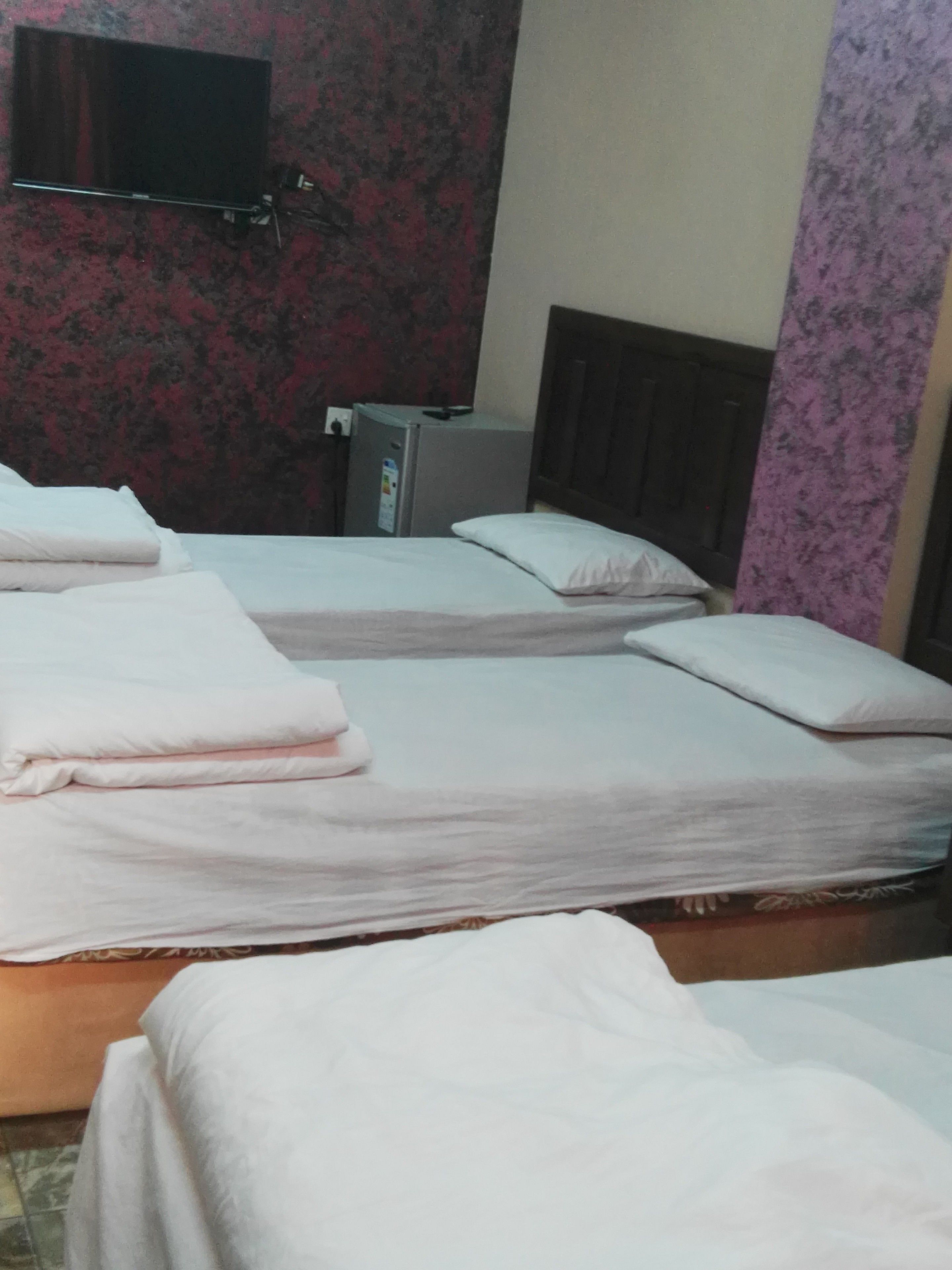 A hotel room with three beds, a television on the wall, and a refrigerator.