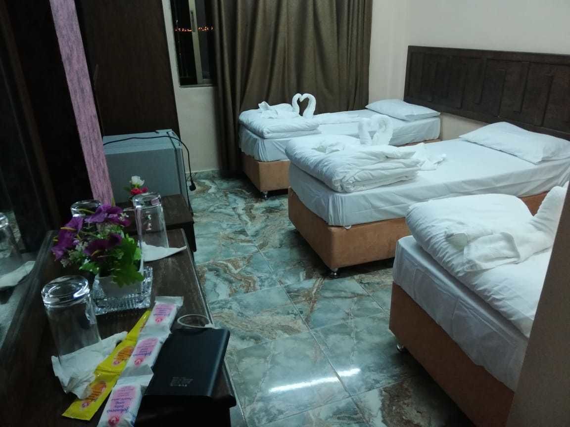 A hotel room with two beds, a wooden headboard, a marble floor, a small table with a vase of flowers, and a mirror.