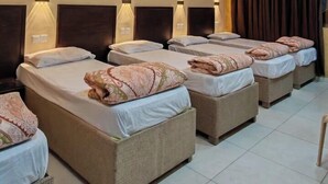 Quarto de hotel com várias camas, ventoinha no teto e iluminação embutida na parede.