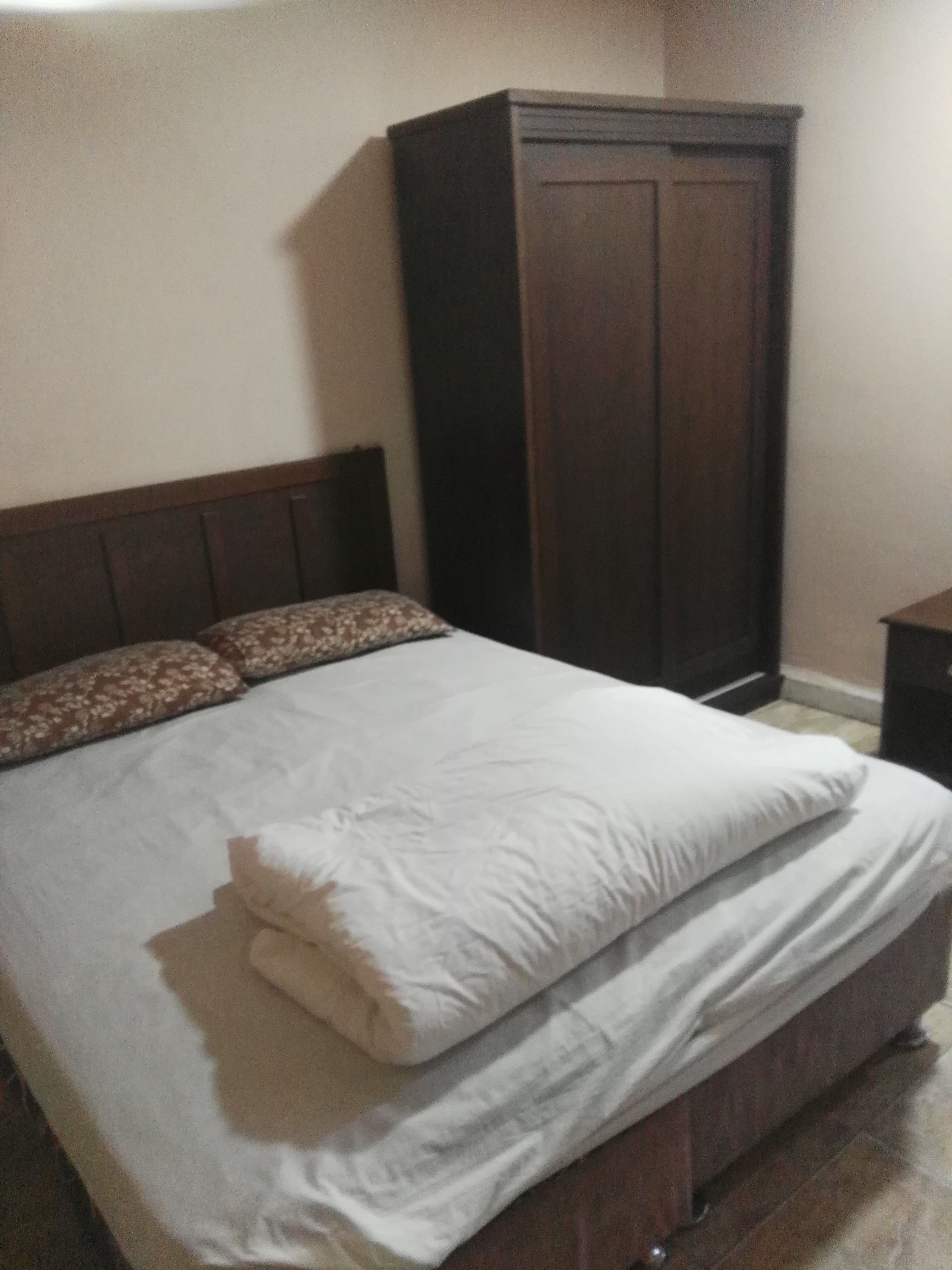 Un dormitorio con cama, armario de madera y mesita de noche.