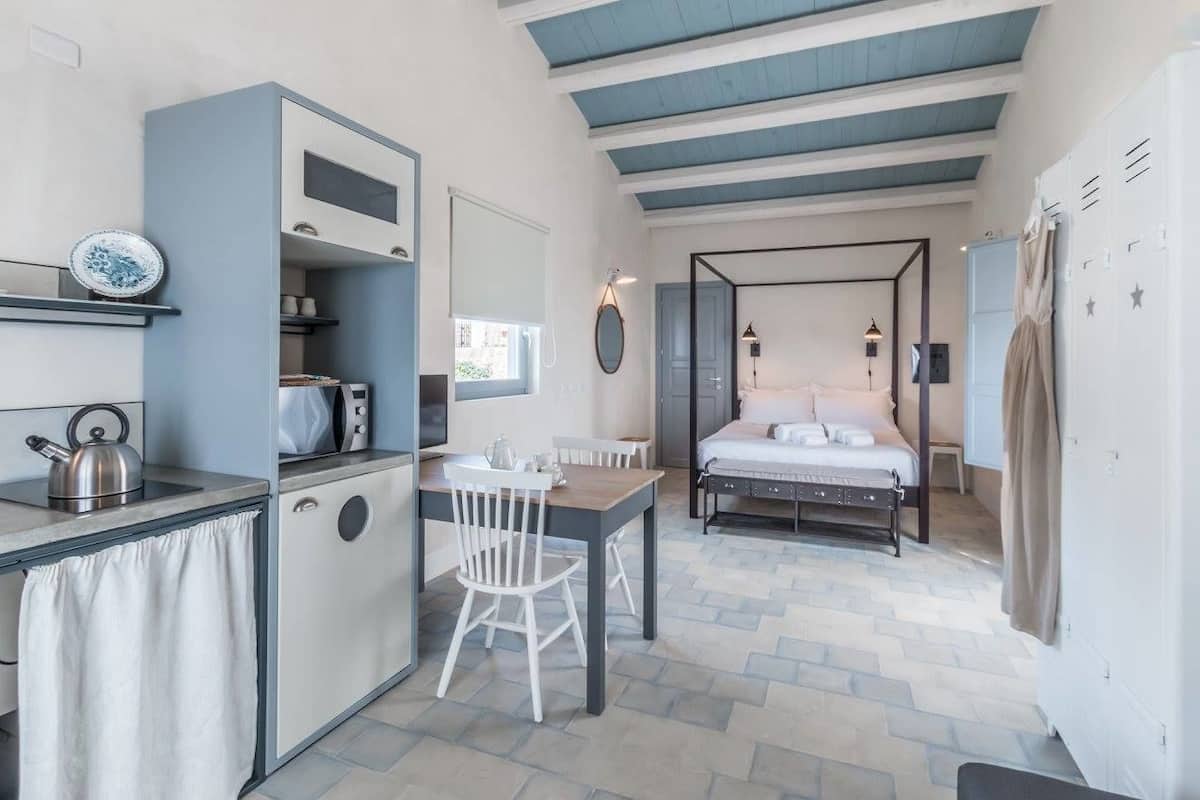 A compact room with a kitchenette, a bed with a canopy, and a small dining area.