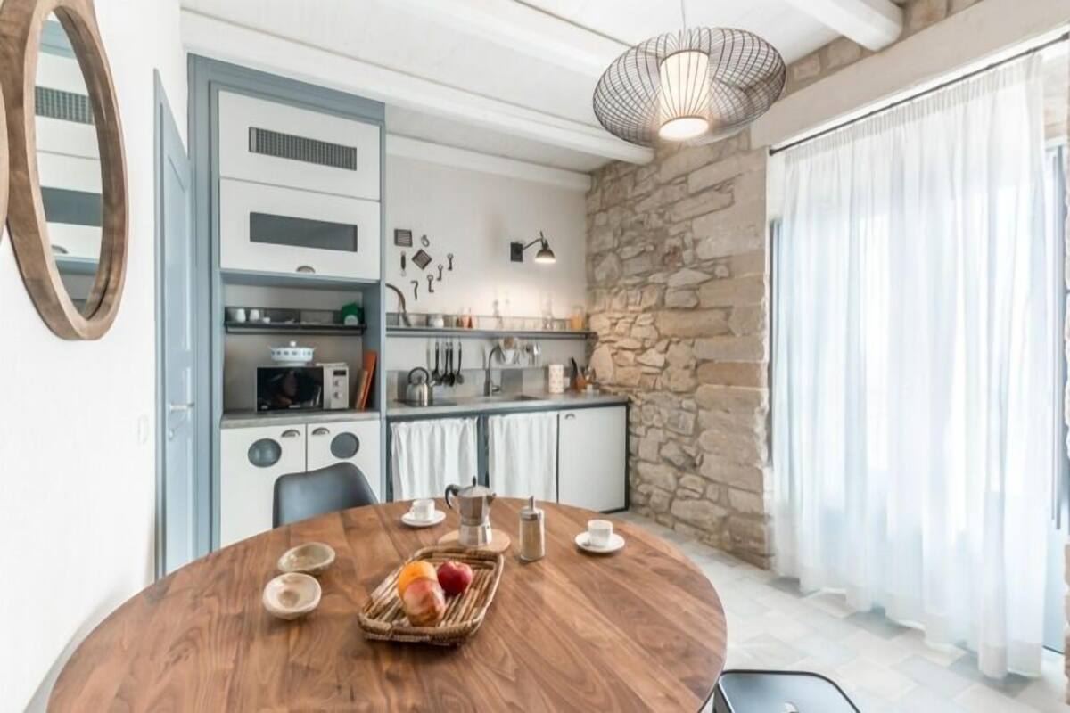 A modern kitchen with a stone wall, a dining table with fruit, and a hanging light fixture.