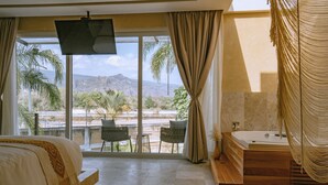 A bedroom with a large bed, a bathtub, and a balcony with chairs.