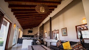 A spacious living area with a high ceiling, a sofa set, a dining table, and a kitchen in the background.