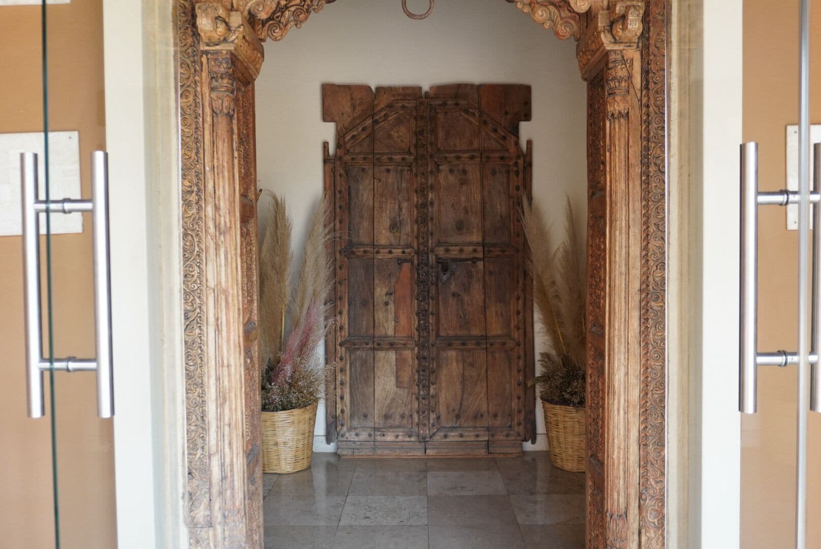 An ornate wooden door with a rustic design, flanked by two wicker baskets with dried plants.