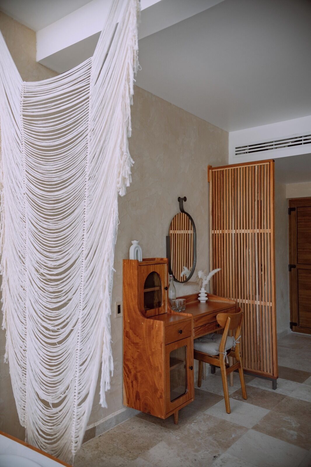 Une pièce avec un bureau en bois, un miroir et une décoration murale en macramé.