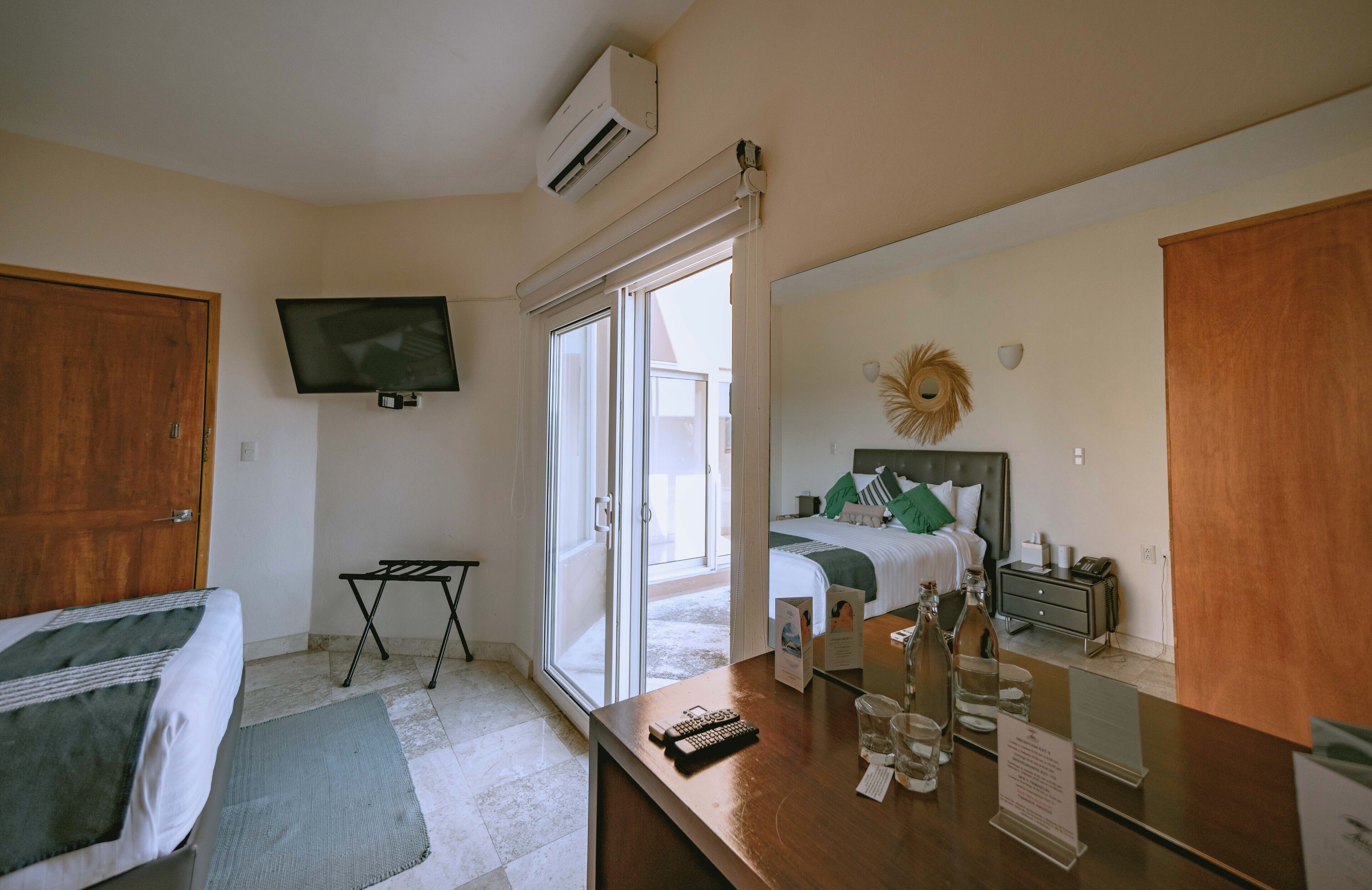Une chambre d’hôtel comprenant un lit, un bureau avec un miroir, une télévision et une porte-fenêtre coulissante donnant sur un balcon.