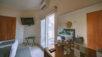 A hotel room with a bed, a desk with a mirror, a television, and a sliding glass door leading to a balcony.