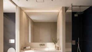 Un baño moderno con un espejo grande, un lavabo blanco y una ducha con cerramiento de vidrio.