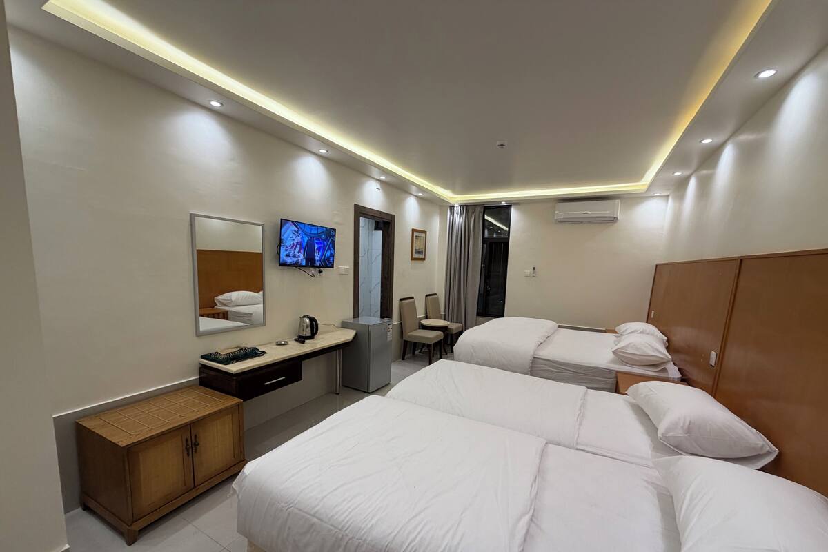 A hotel room with two beds, a desk with a computer, a television, and a wardrobe.