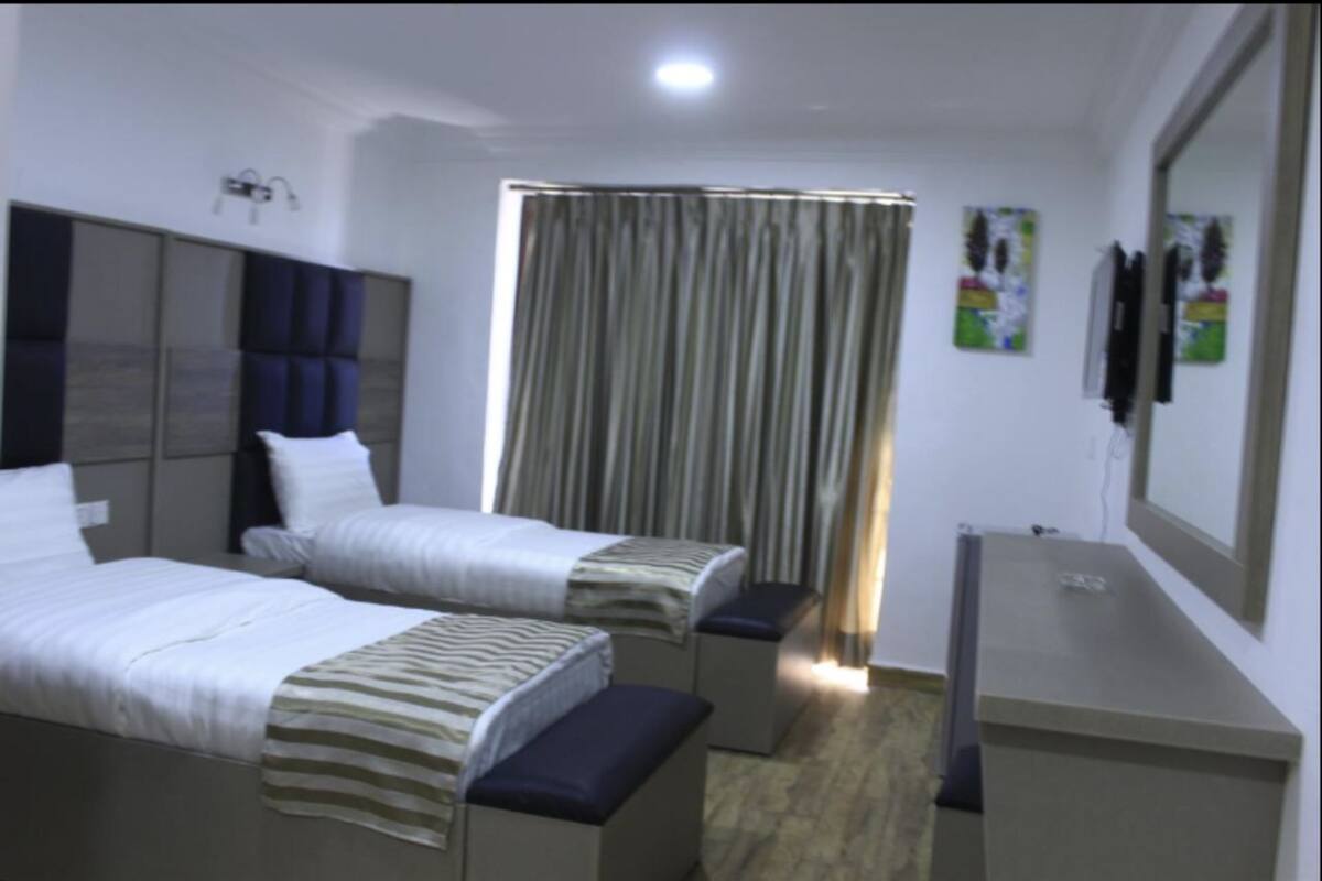 A hotel room with two beds, a desk, a mirror, and a curtain.