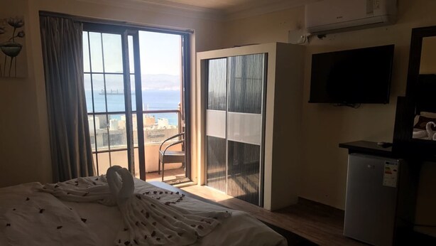 A hotel room with a bed, a TV, a desk, and a view of the sea. - Ahla Tlah SeaView Hotel (Aqaba)