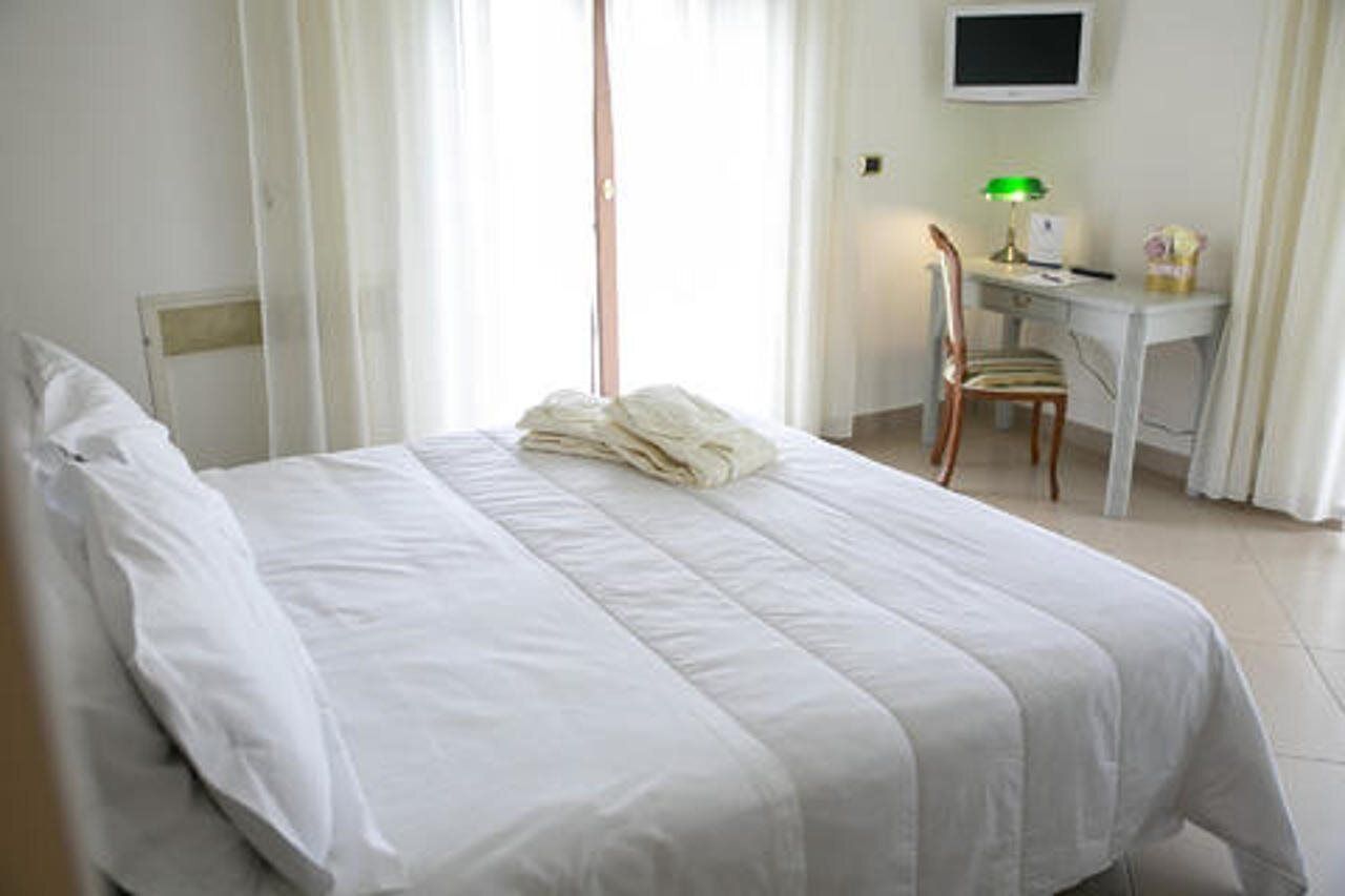 Una habitación de hotel con cama, escritorio, silla, televisor y lámpara.