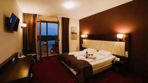 Habitación de hotel con cama, escritorio, televisión y balcón con vistas.