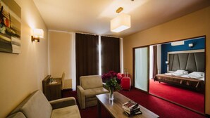 Una habitación de hotel con cama, sofá, una mesa con un jarrón de flores y una ventana con cortinas.