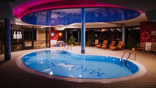 Una piscina con zona de borde, sillas de descanso y un techo con diseño ondulado.