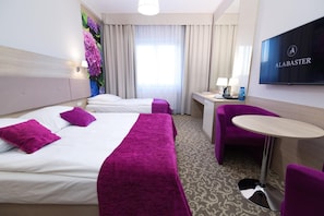 A hotel room with two beds, a desk, a chair, a TV, and a window with curtains.