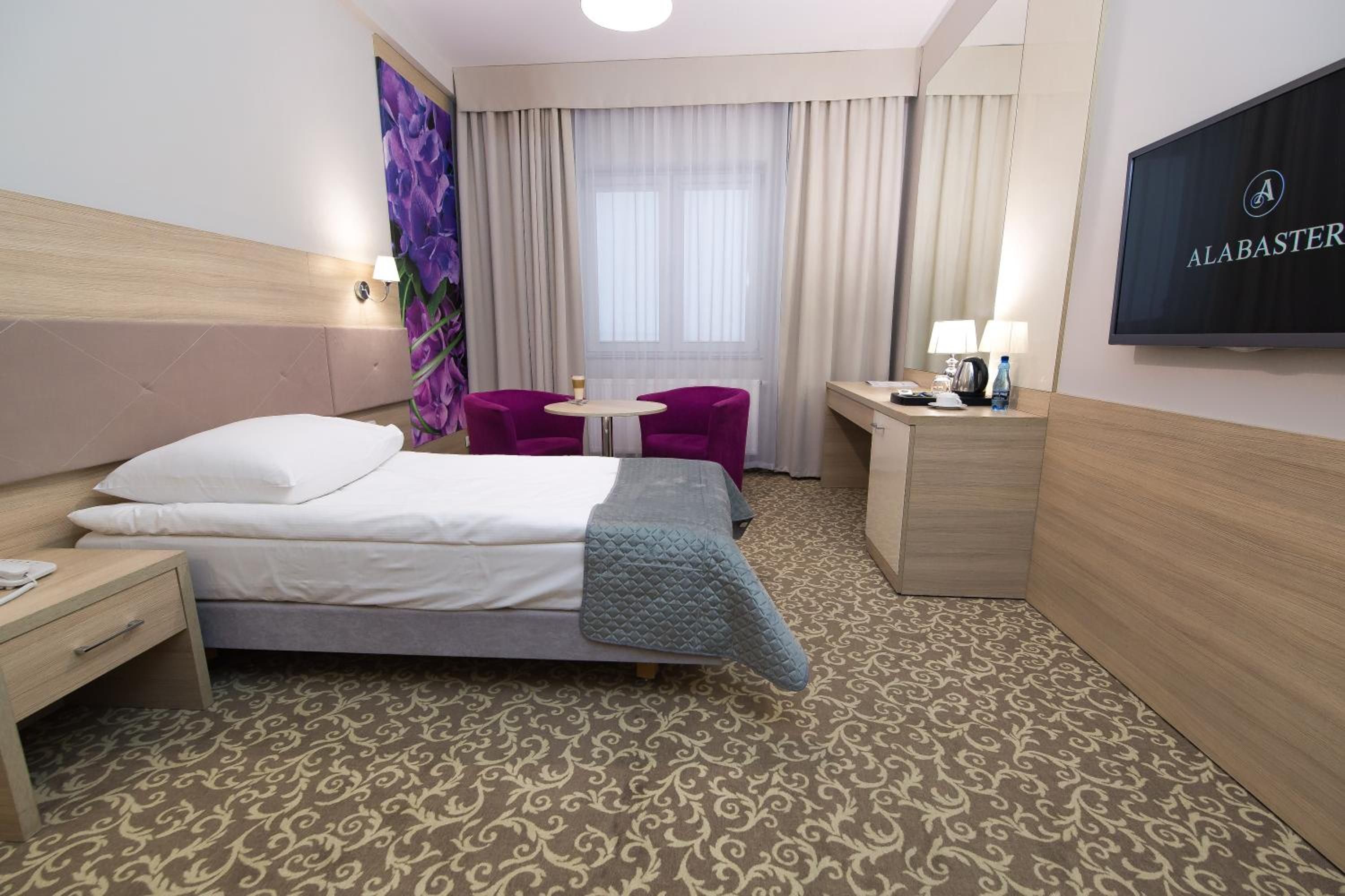 Una habitación de hotel con cama, escritorio, silla, televisión y ventana con cortinas.