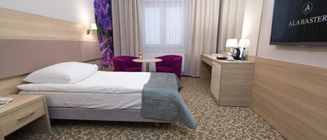 Una habitación de hotel con cama, escritorio, silla, televisión y ventana con cortinas.