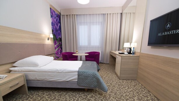 A hotel room with a bed, a desk, a chair, a TV, and a window with curtains.