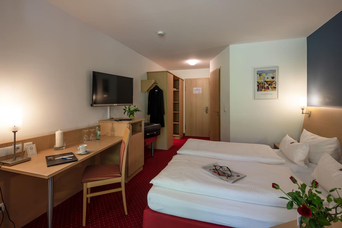 A hotel room with a bed, a desk, a chair, a television, and a wardrobe.