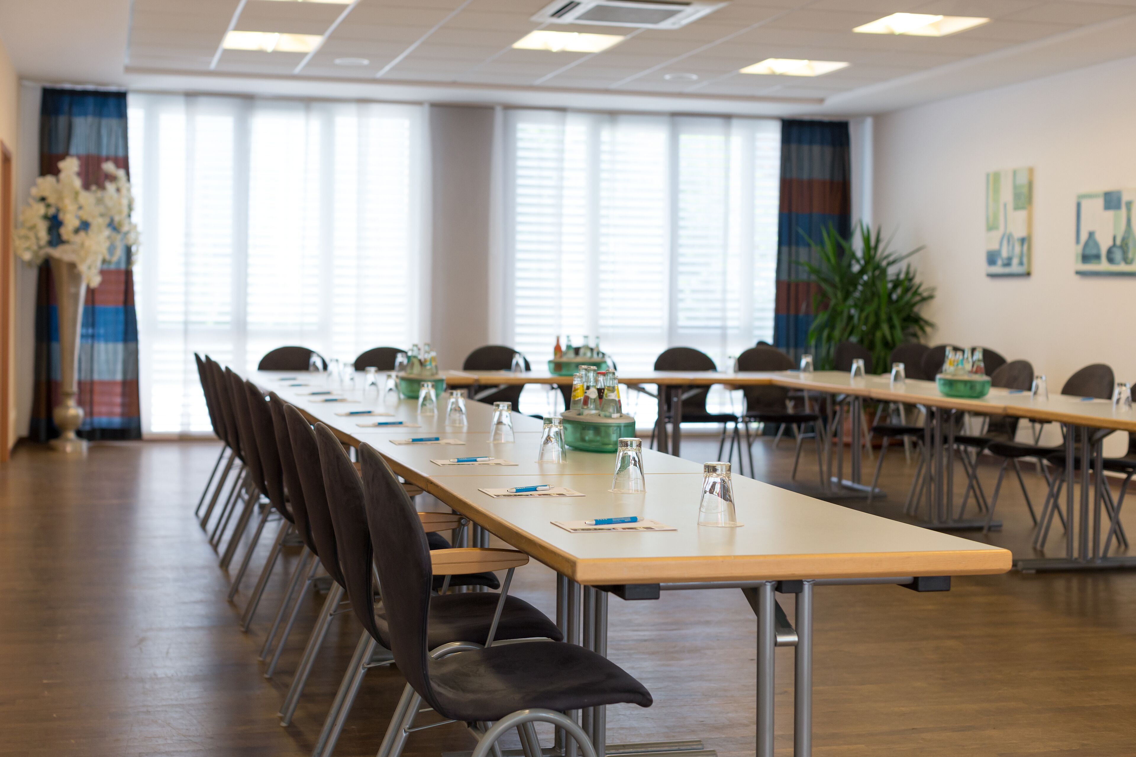 Ein Konferenzraum mit langen Tischen, Stühlen und einem großen Fenster mit Jalousien.