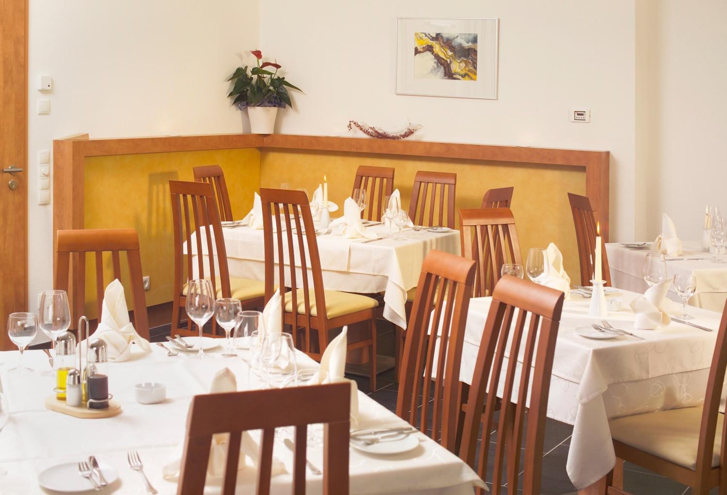 Comedor con sillas y mesas de madera, manteles blancos y velas.