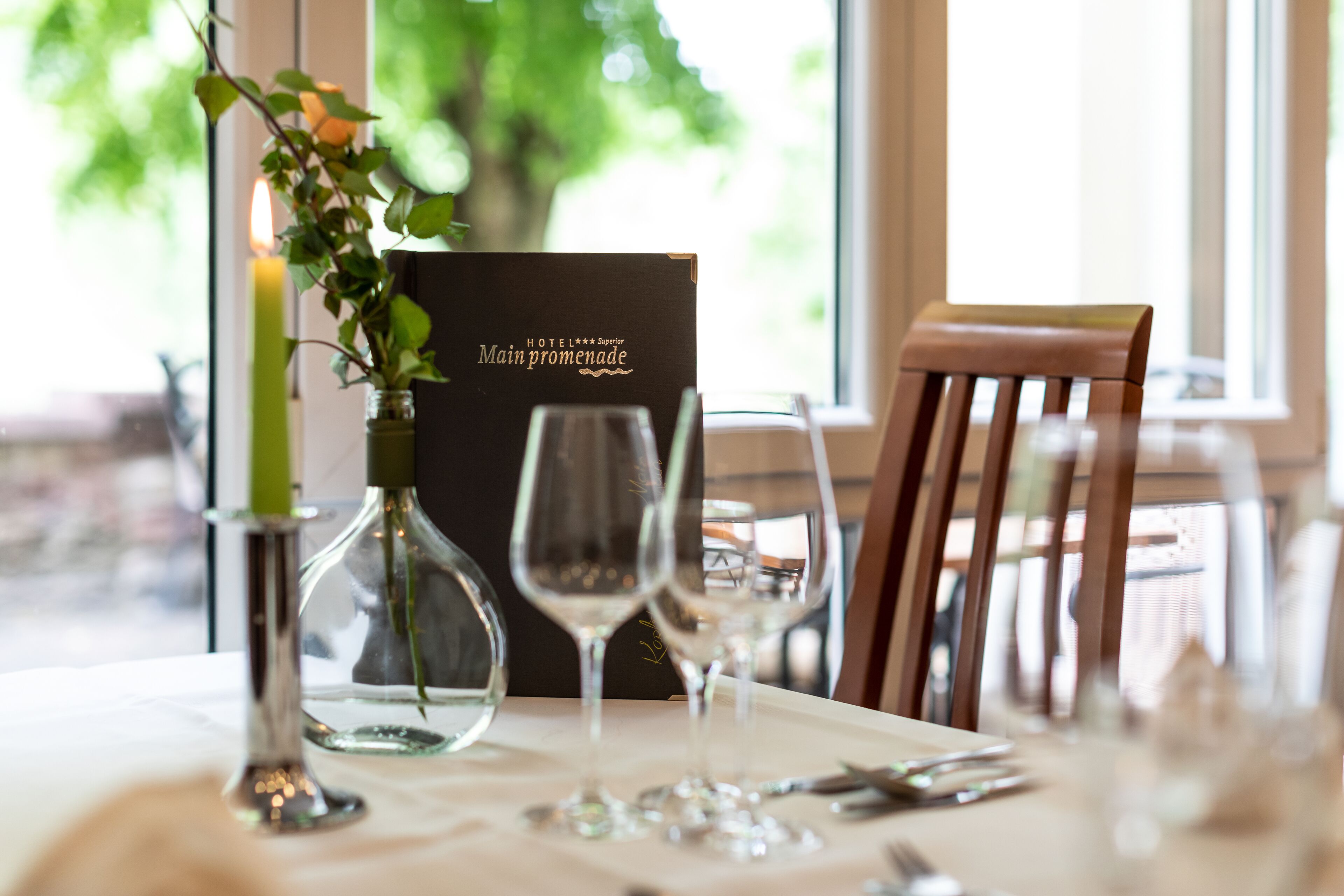 A dining table set with wine glasses, a candle, and a menu.