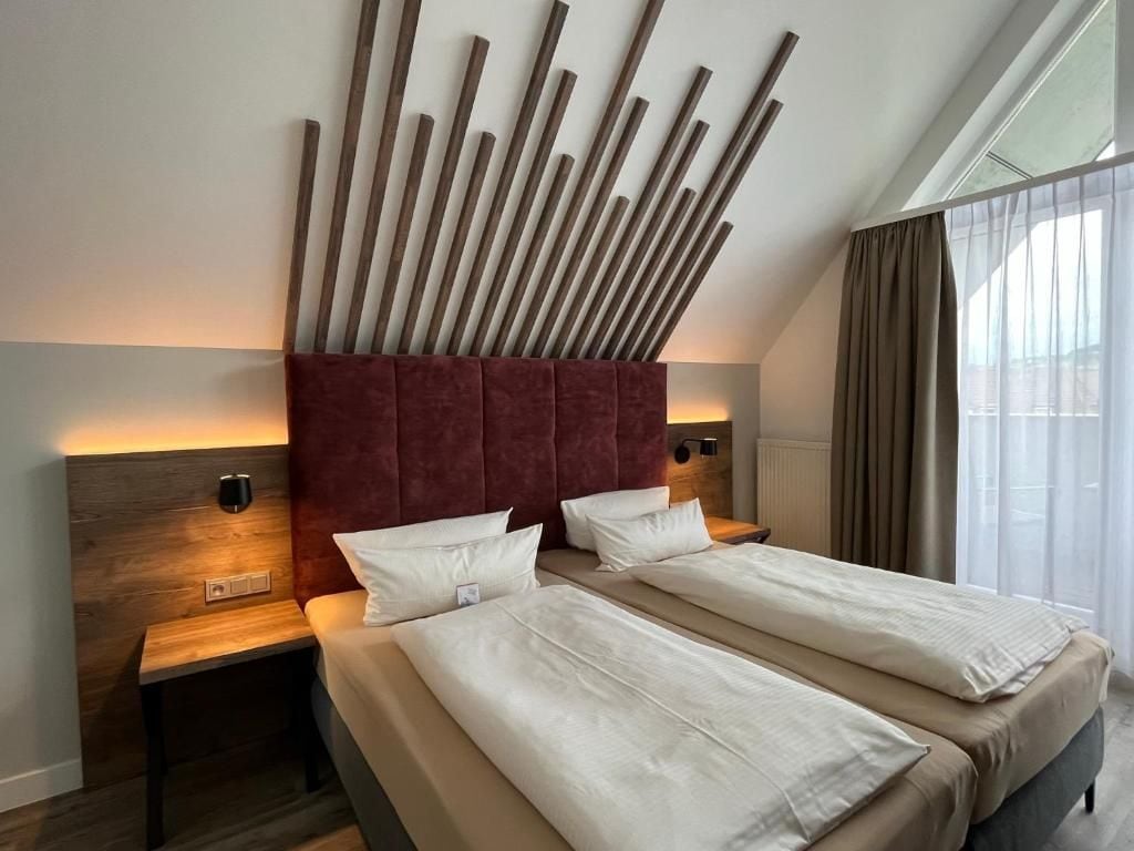 Una habitación de hotel con una cama, dos mesitas de noche, una lámpara de pared y una ventana con cortinas.