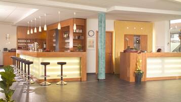 A modern hotel lobby with a reception desk, bar area, and seating.
