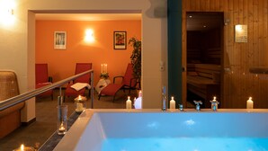 Et spa-område med et stort badekar, trævægge og et loungeområde med stole og et bord.