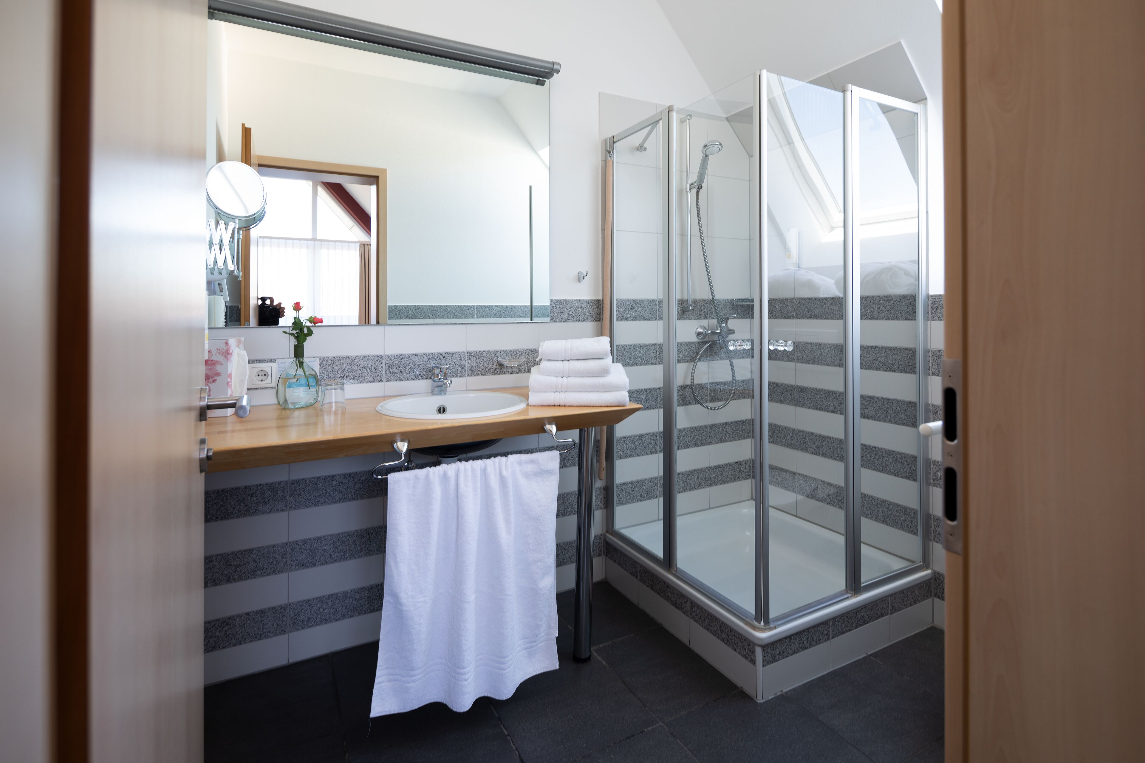A modern bathroom with a glass shower enclosure, a vanity with a sink, and a large mirror.