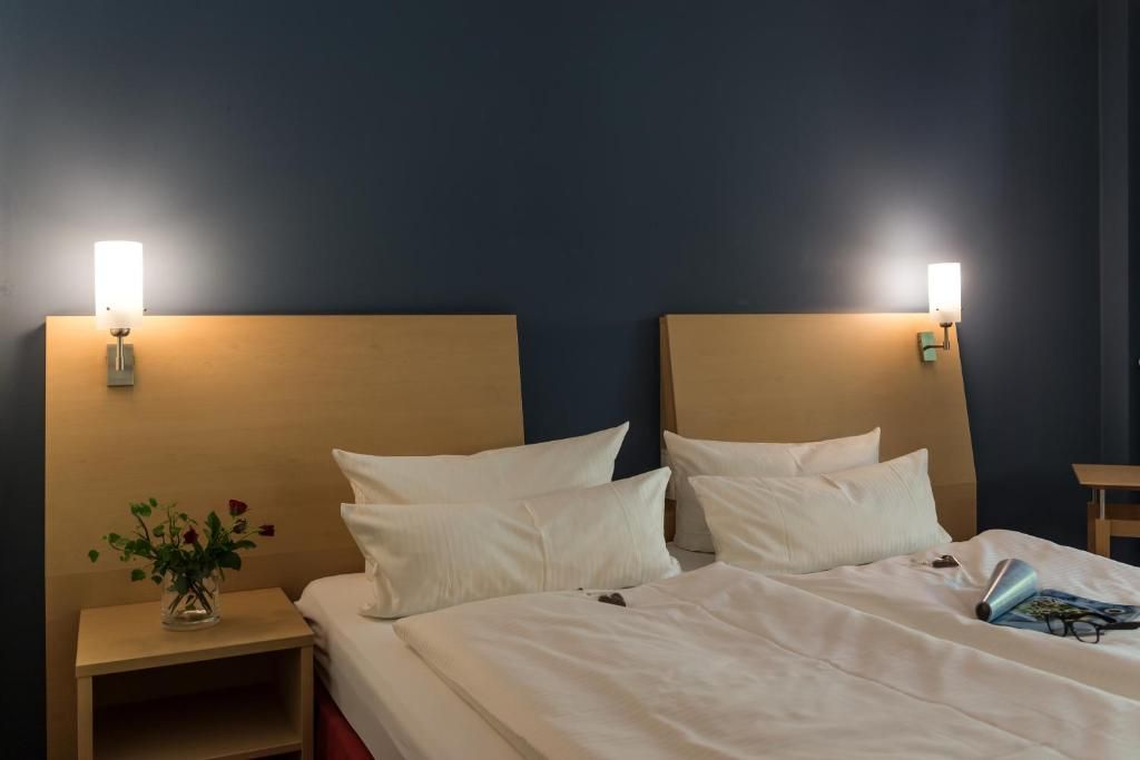 A hotel room with a bed, bedside tables, and wall-mounted lamps.