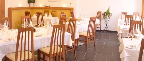 Un coin repas avec des chaises et des tables en bois, préparé pour un repas, agrémenté d’un arrangement floral central et d’un tableau au mur.