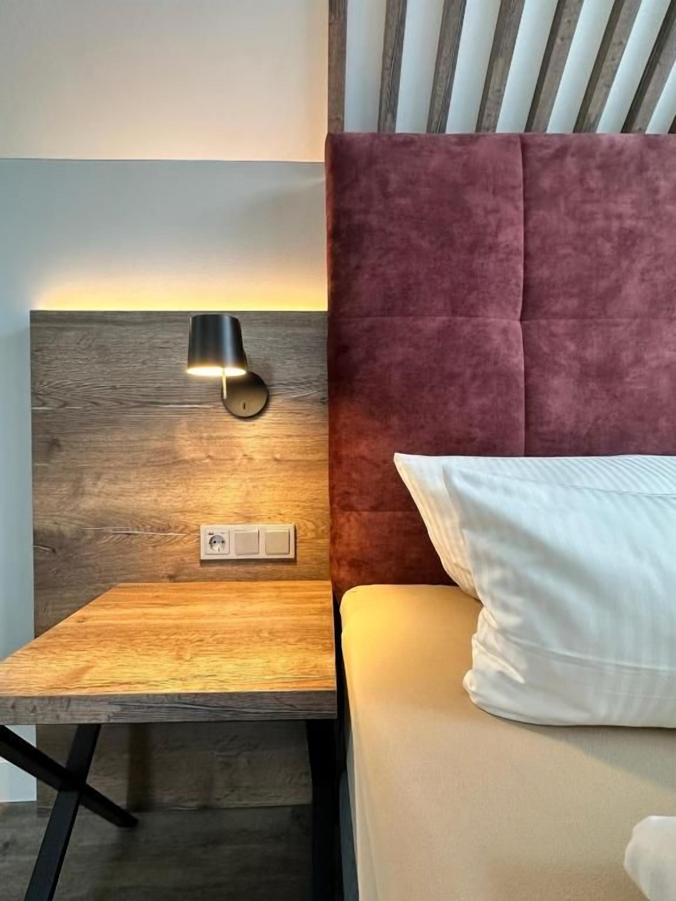 Una cama con cabecera, una mesita de noche y una lámpara de pared.