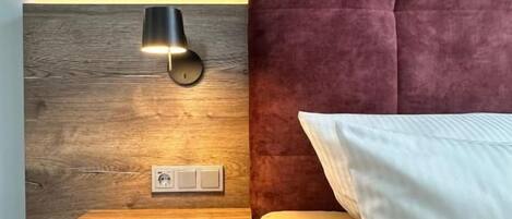 Una cama con cabecera, una mesita de noche y una lámpara de pared.