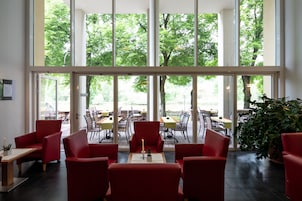 Uma sala de jantar moderna, com cadeiras e mesas vermelhas, e grandes janelas com vista para o verde lá fora.