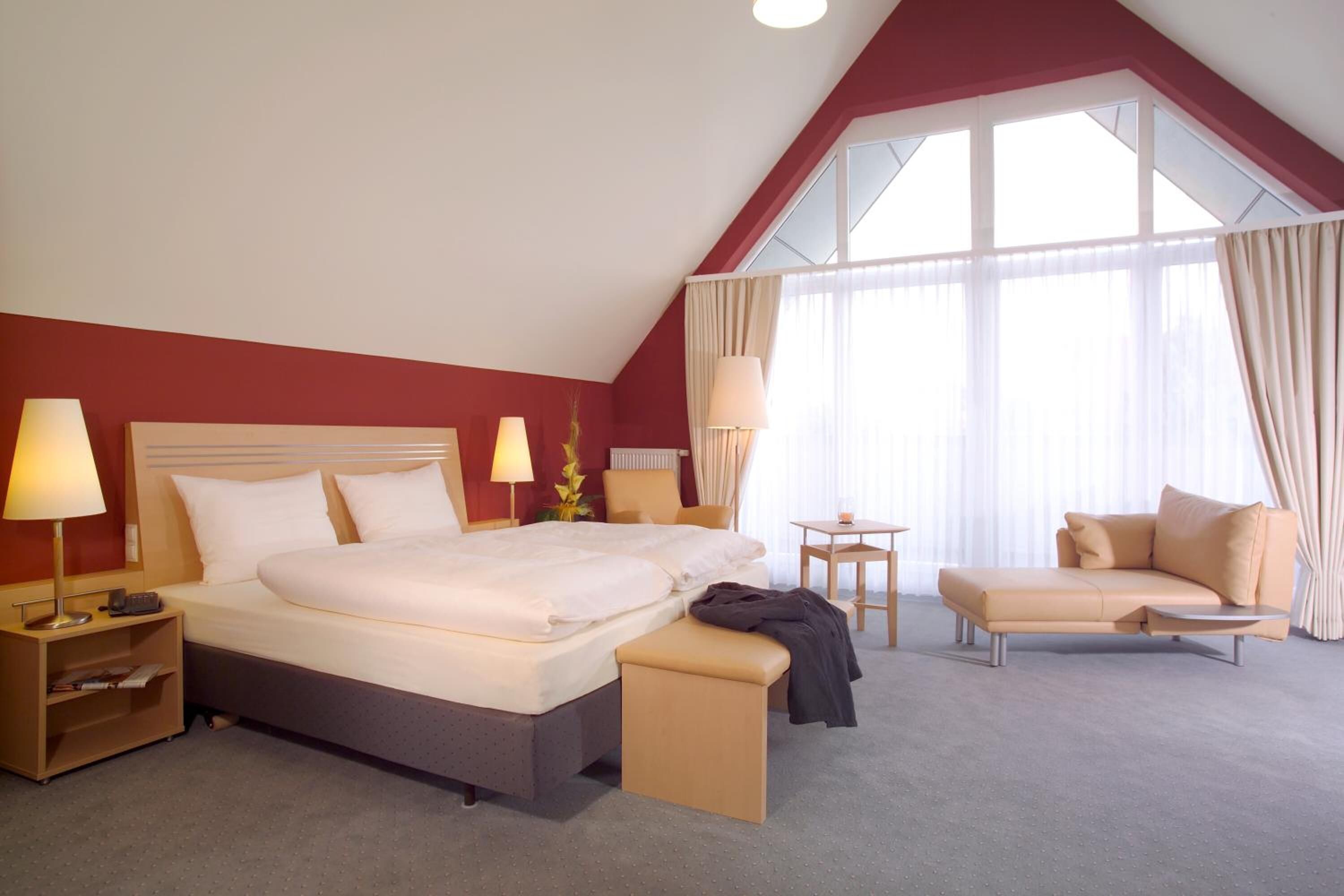 A hotel room with a large bed, bedside tables, a desk, a chair, and a window with curtains.