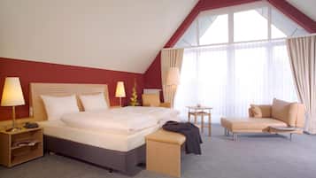 A hotel room with a large bed, bedside tables, a desk, a chair, and a window with curtains.