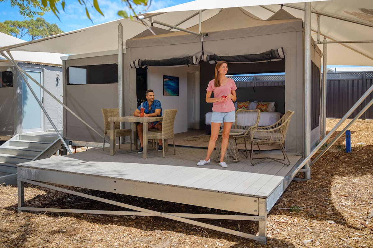 A covered outdoor area with a table and chairs, a bed, and a small staircase leading to a door.