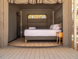 Tienda de campaña compacta y bien iluminada con una cama individual, una mesita y un ventanal que ofrece vistas al exterior.
