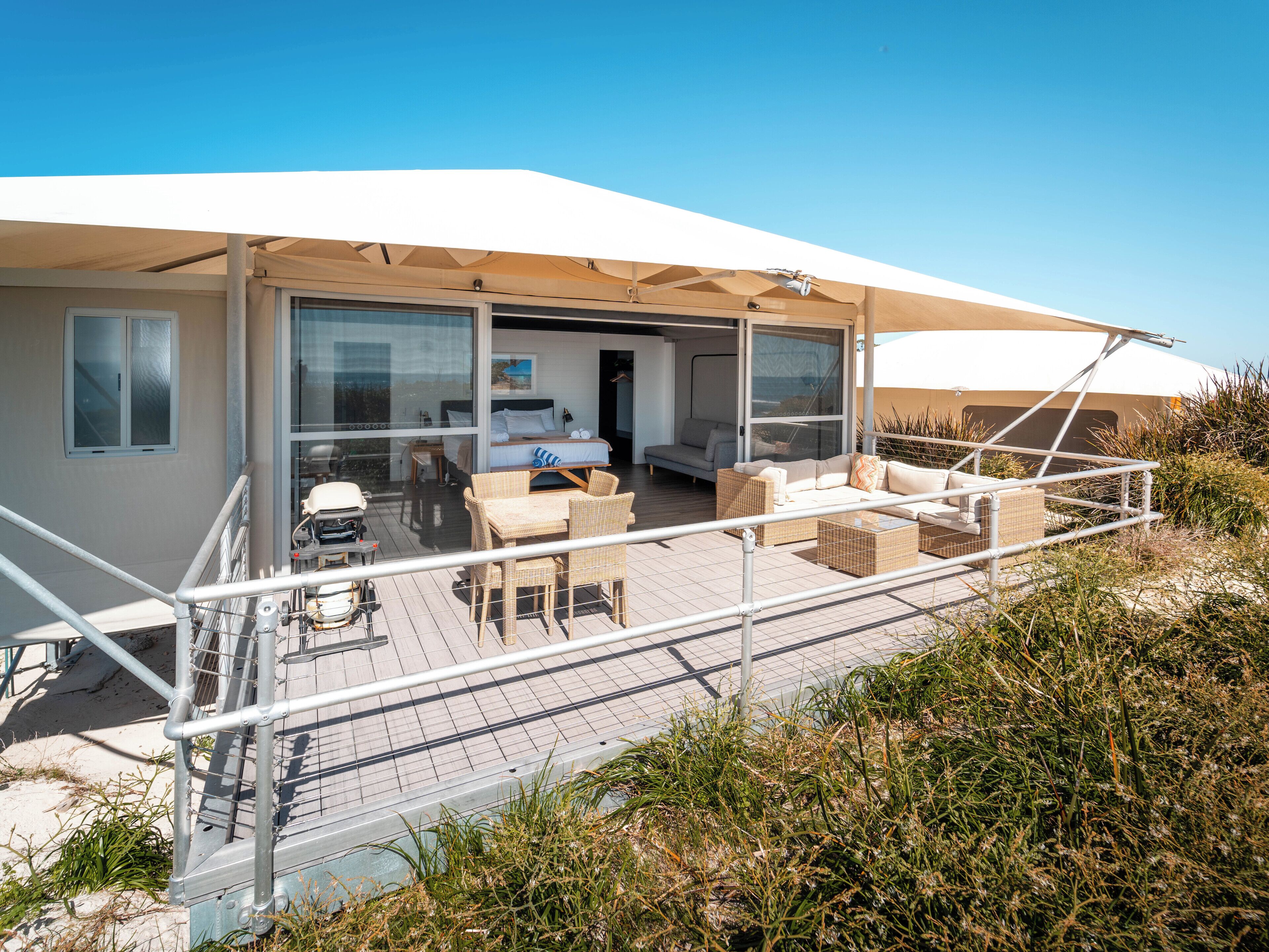 A modern, open-plan living area with a large sliding glass door leading to a bedroom, furnished with wicker furniture and a white canopy overhead.