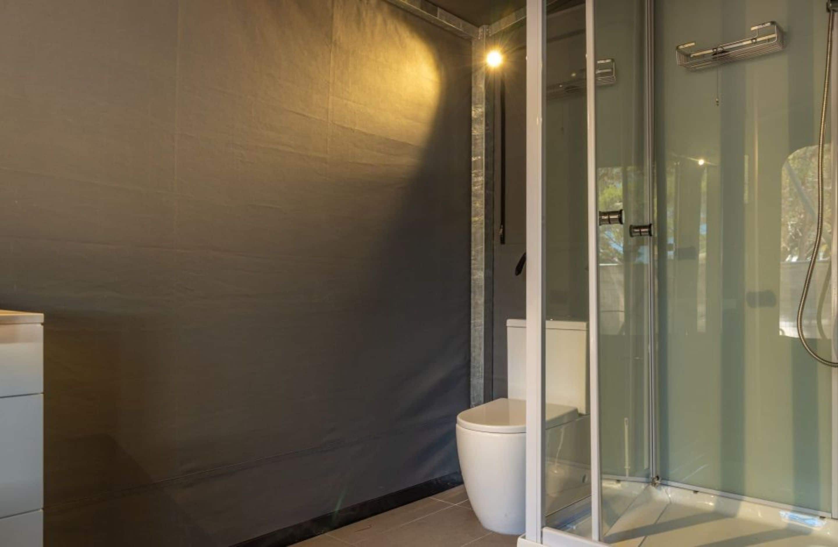 Une salle de bain moderne avec une douche à parois de verre, des toilettes blanches et un mur texturé de couleur foncée.