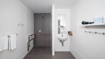 A modern bathroom with a shower, a sink, and a mirror. There is a towel rack and a shelf with toiletries.