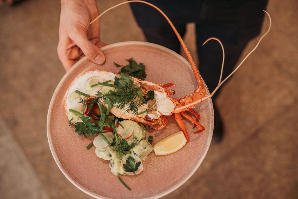 Une personne tenant une assiette avec un homard, une salade et une tranche de citron.