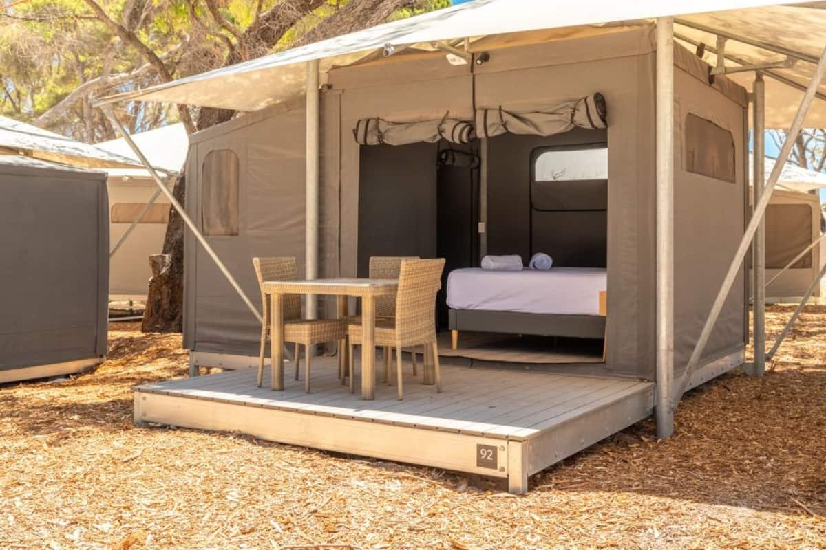 A portable tent with a bed, a table, and chairs, set on a wooden deck.