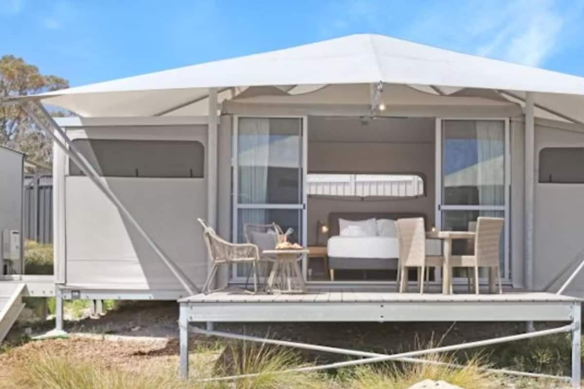 A modern tent-style accommodation with a balcony, a bed, and a dining area.